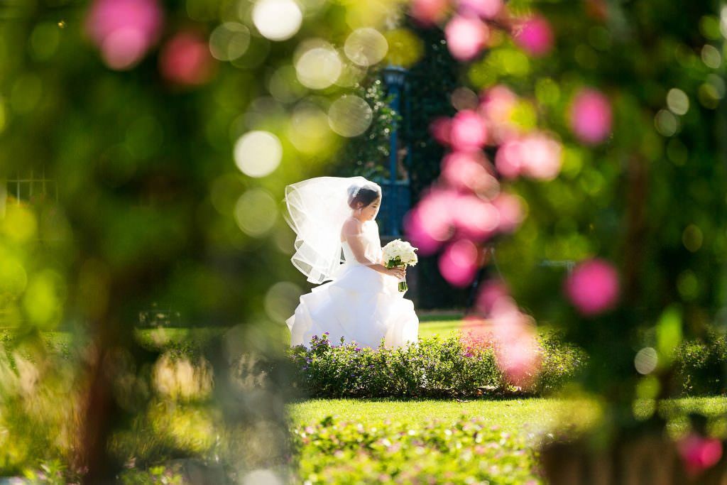 A bride in a wedding dress is standing in a garden holding a bouquet of flowers.