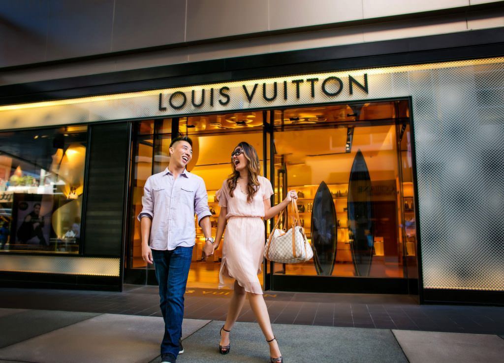 Eclectic Engagement Portraits In OC A fun engagement portrait of a couple walking in front of a louis vuitton store
