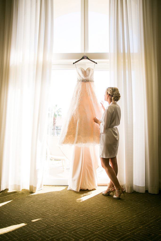 A bride is looking at her wedding dress hanging in a window at Hyatt Regency Huntington Beach.
