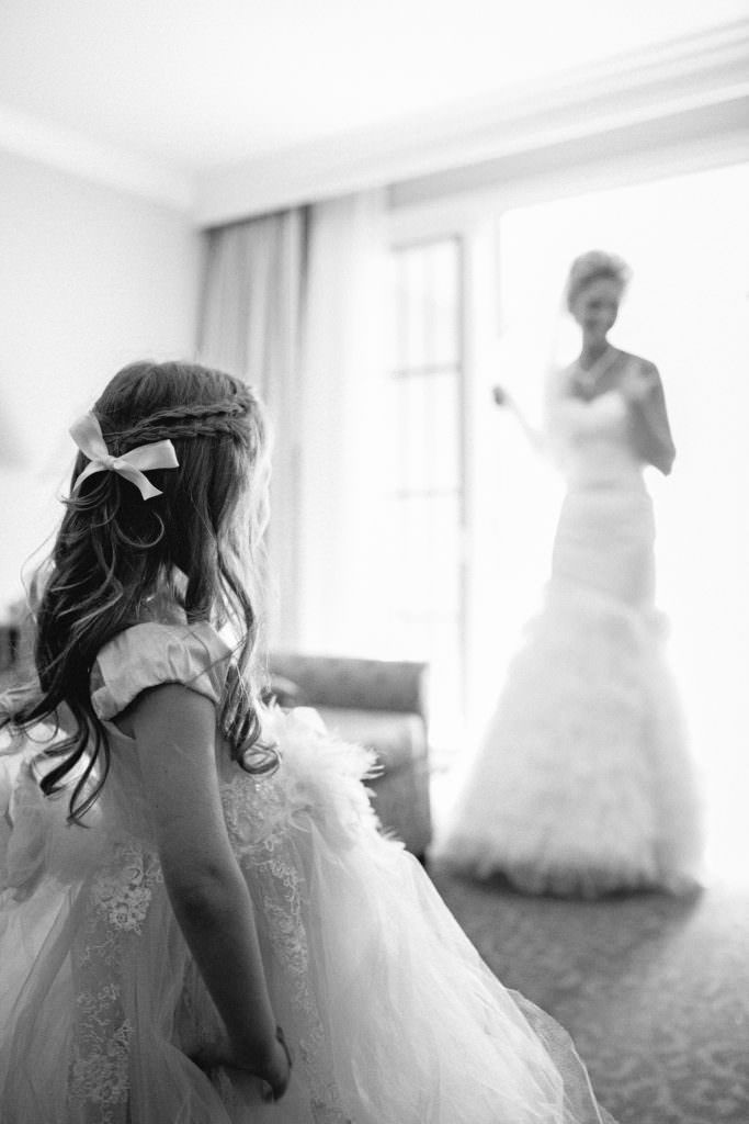 A flower girl is standing in front of a bride in a wedding dress in San Juan Capistrano.