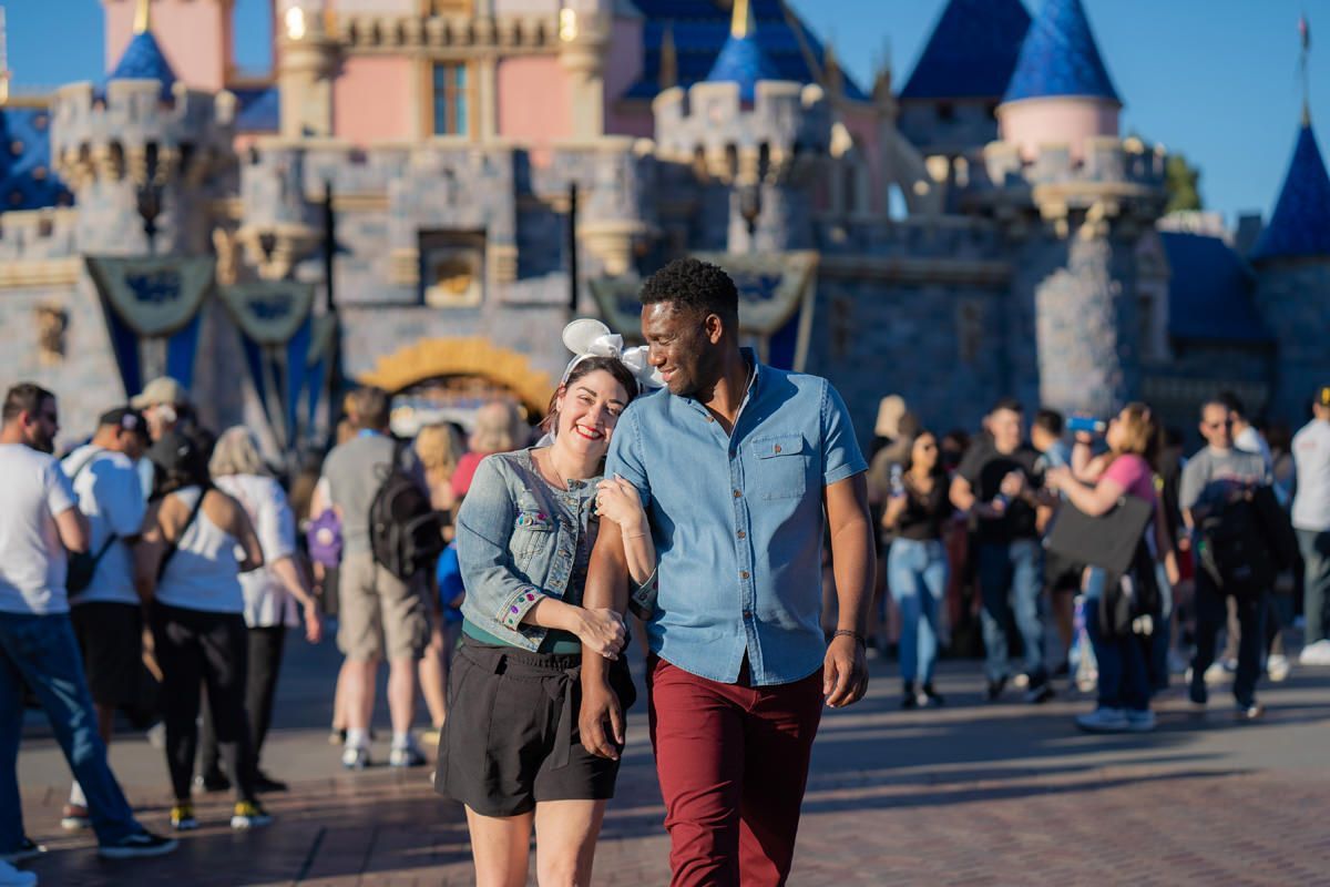 A man and a woman are walking in front of a castle at Disneyland.