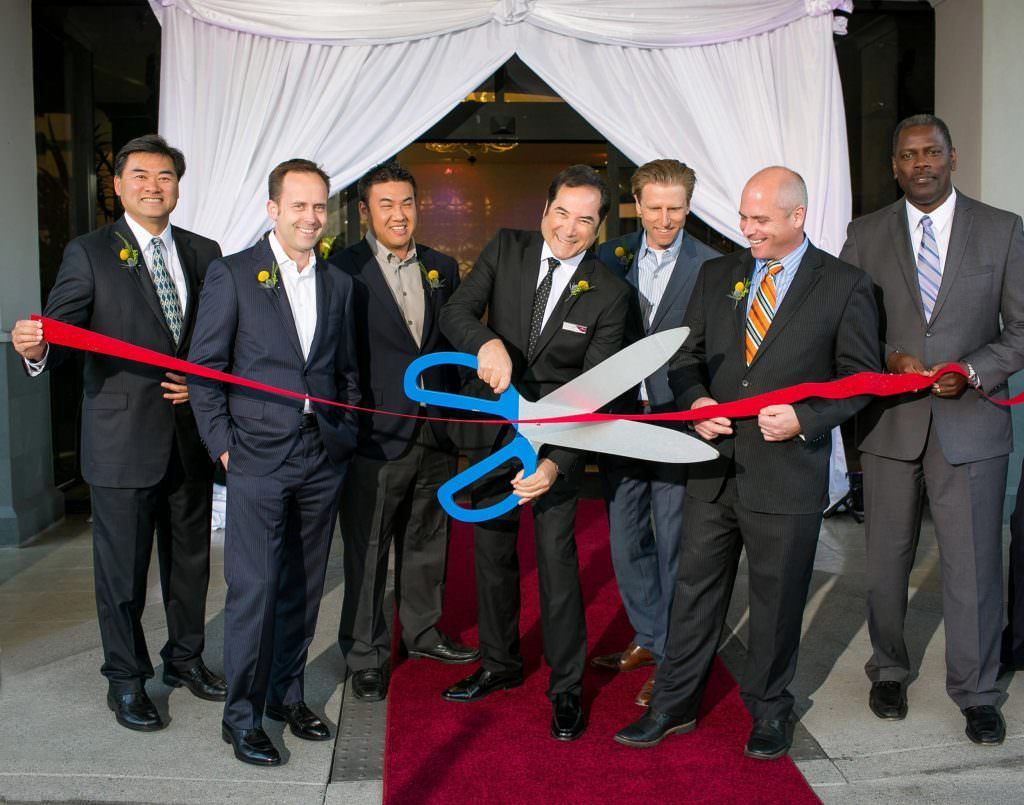 Event Photo of Ribbon Cutting Ceremony A group of men in suits are cutting a red ribbon with giant scissors