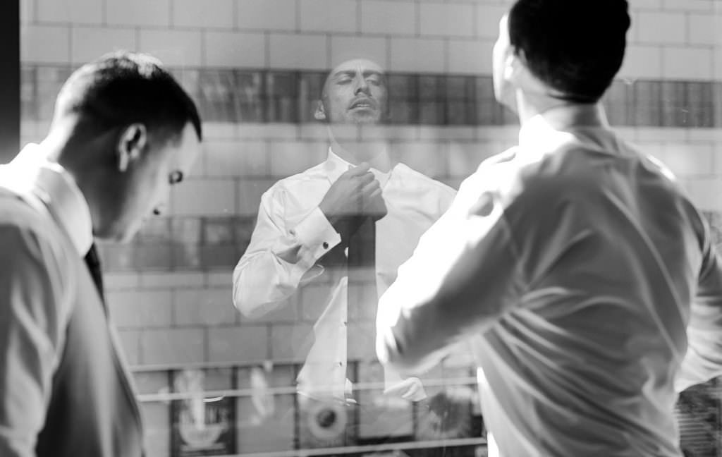 a groom is looking at his reflection in a mirror.