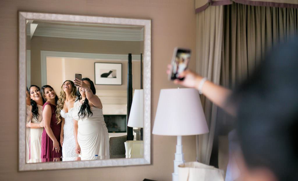 A bride is taking a picture of her bridesmaids in front of a mirror at the Montage Resort.
