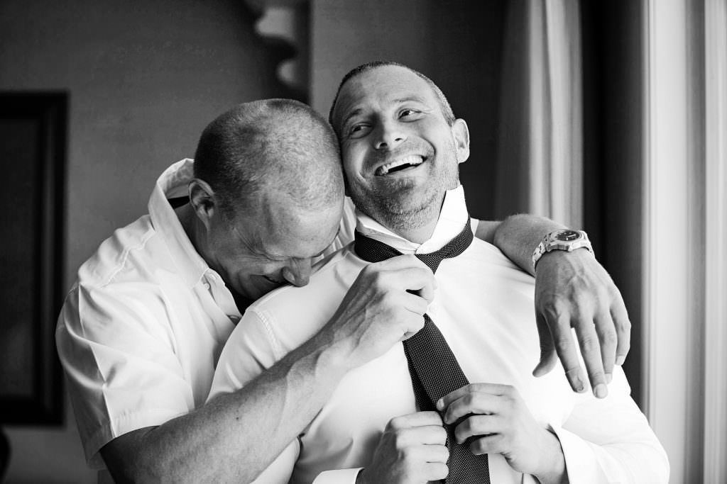 A man is helping a groom tie his tie before his wedding Hyatt Huntington Beach