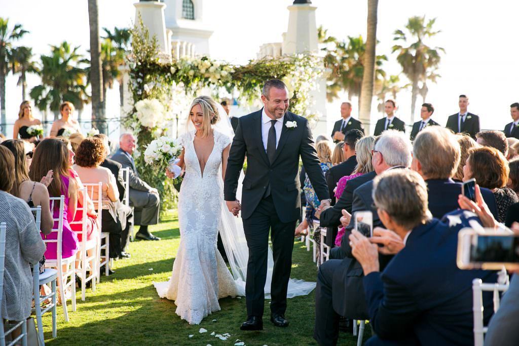 A bride and groom are walking down the aisle at their wedding holding hands at the lighthouse Courtyard in Huntington Beach.