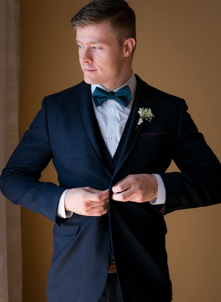 A groom in a suit and bow tie is adjusting his jacket.