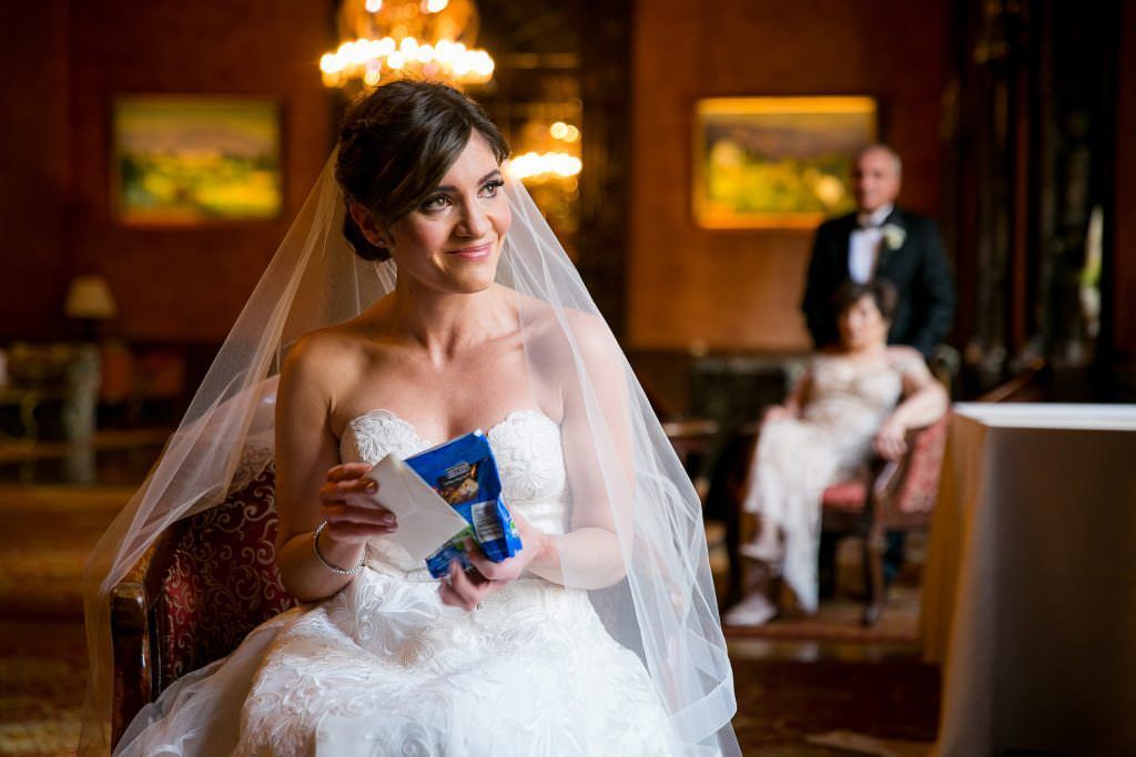A bride in a wedding dress is sitting in a chair holding a card at the Jonathan Club in Downtown LA.