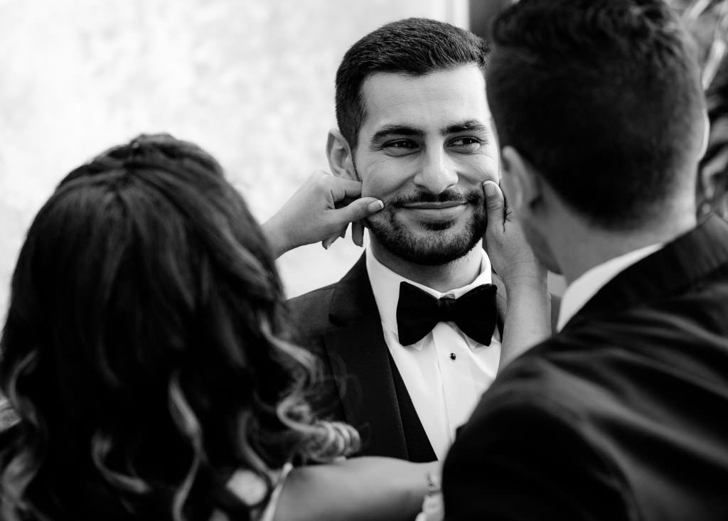 A man in a tuxedo and bow tie is having his cheeks squeezed by his siblings at Westin Costa Mesa