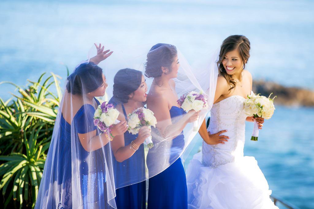 A bride and her bridesmaids are posing for a picture in front of Laguna Beach