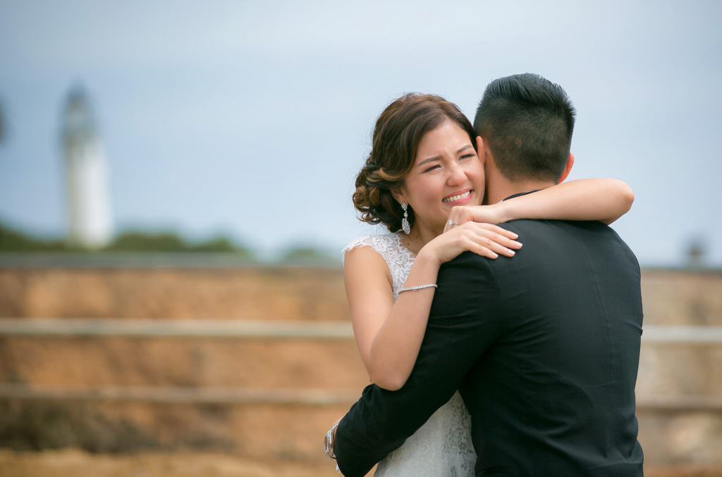 A bride and groom's first look are hugging each other in front of a lighthouse.