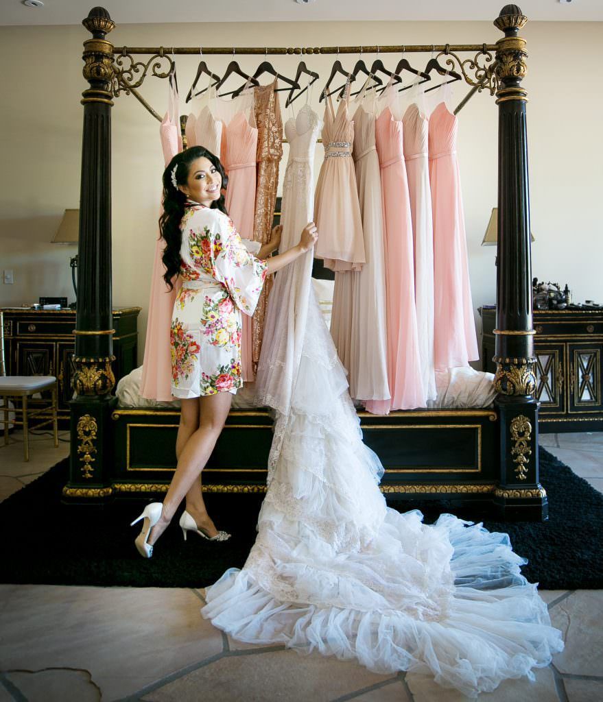 A woman in a robe is standing next to a bed holding a wedding dress at Santiago Mansion in Orange, CA