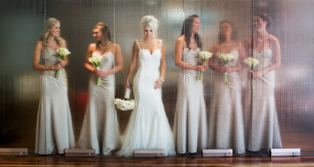 A bride and her bridesmaids are posing for a picture in front of a glass wall at 7° in Laguna Beach