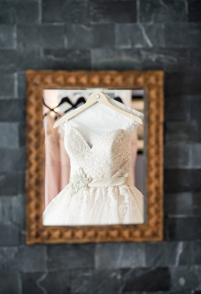 A wedding dress is hanging on a hanger in a mirror at the Portofino in Redondo Beach