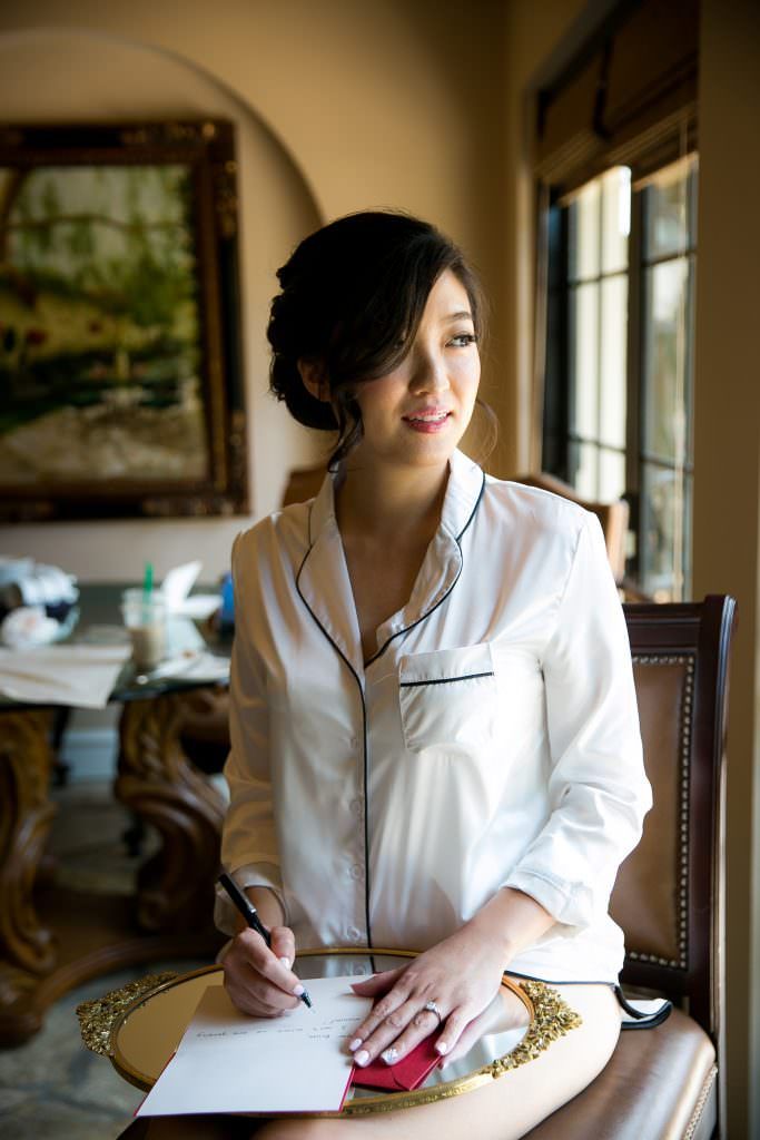 A bride is sitting in a chair writing on a piece of paper.