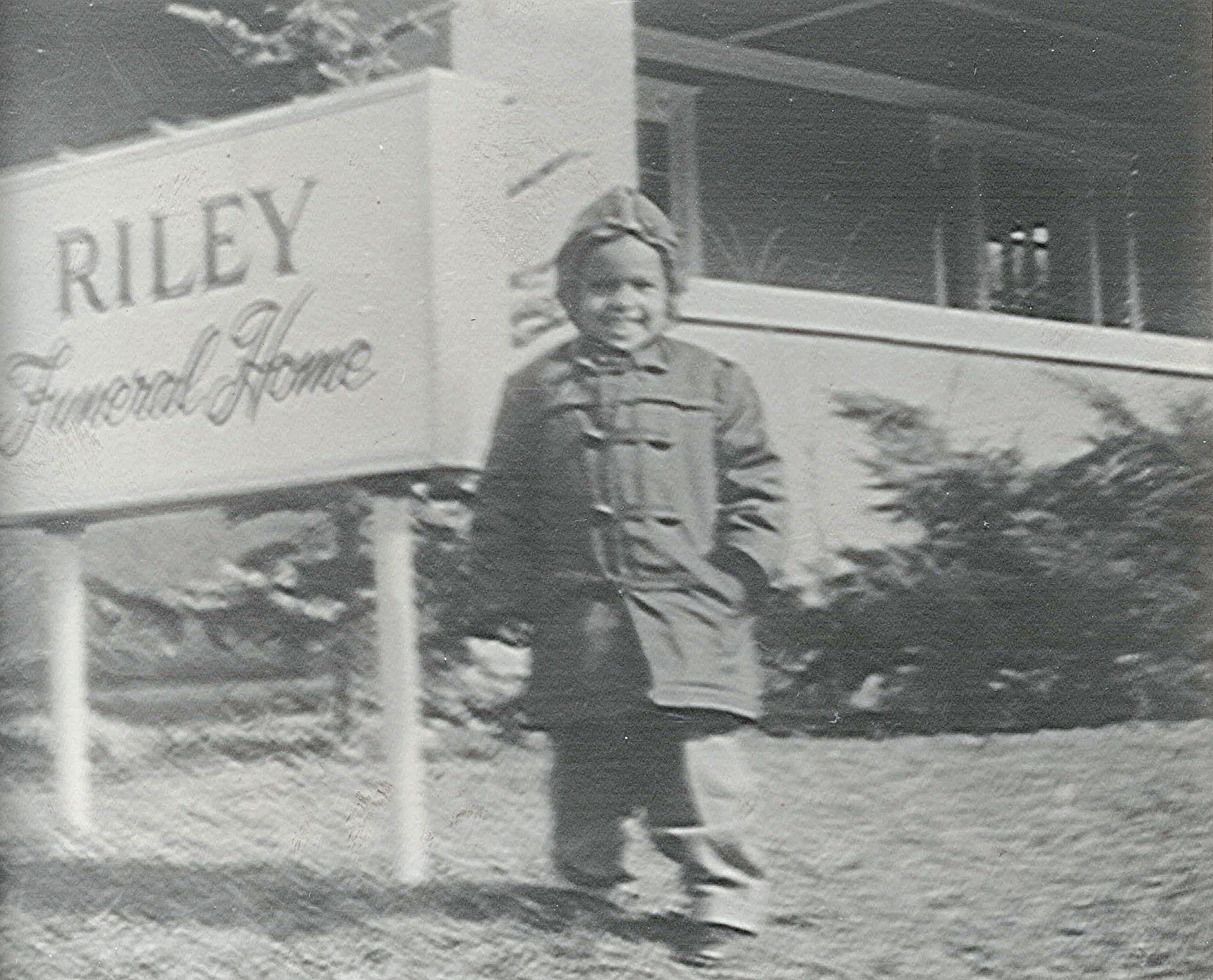 A black-and-white photo in a frame showing a child standing in front of a sign that reads,