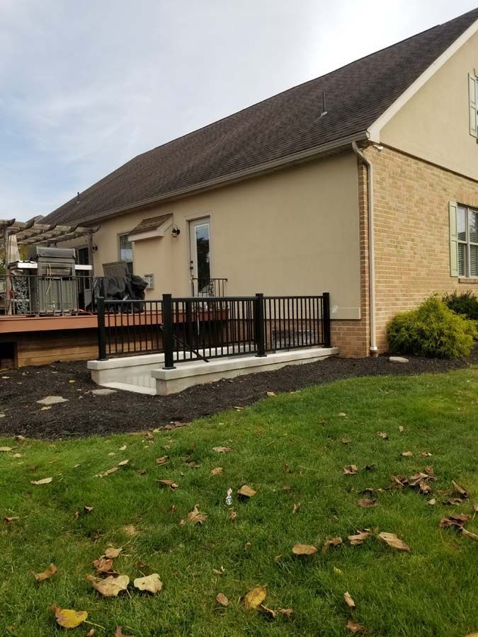 A modern ramp with black metal handrails leading to a wooden deck on the side of a beige residential house.