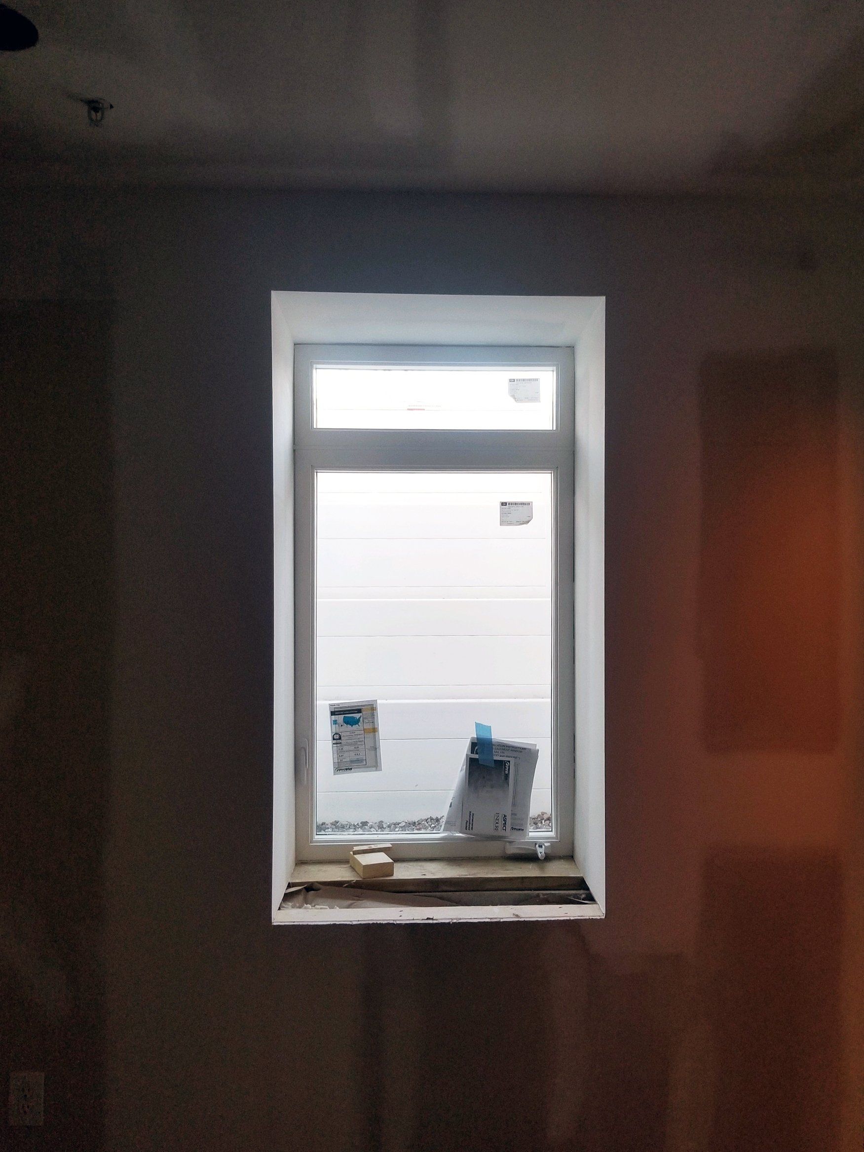 A white-framed window centered on a dark, unfinished interior wall with a narrow sill and construction debris.
