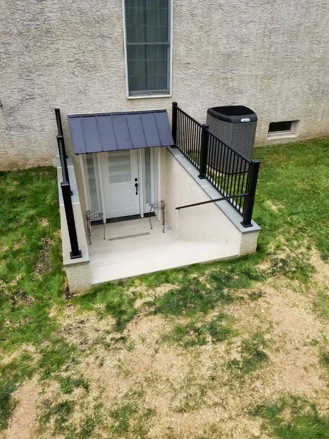 A basement walk-out entrance featuring a white door, a metal awning, and black railings set into a grassy yard.