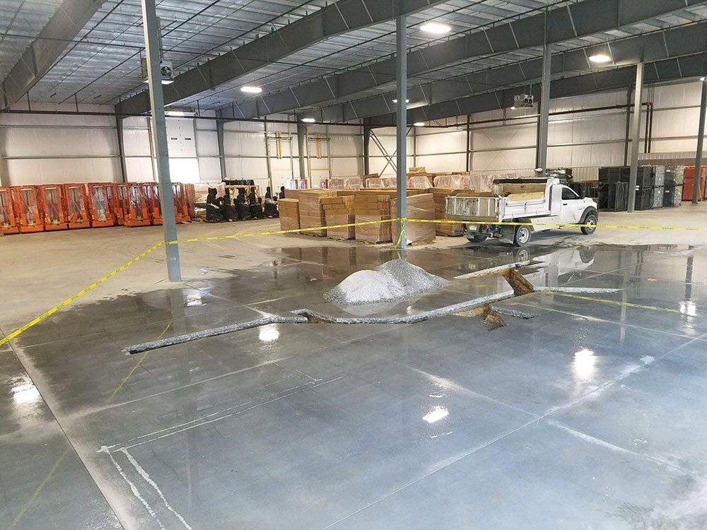 A warehouse interior features a concrete floor with water pooling around a construction pile, cordoned off by yellow tape.