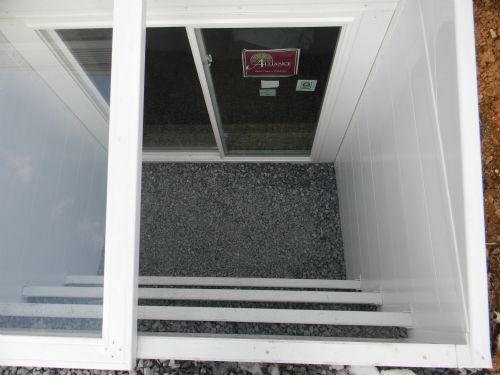 A white egress window well with a sliding glass window, gravel floor, and built-in steps leading up to ground level.