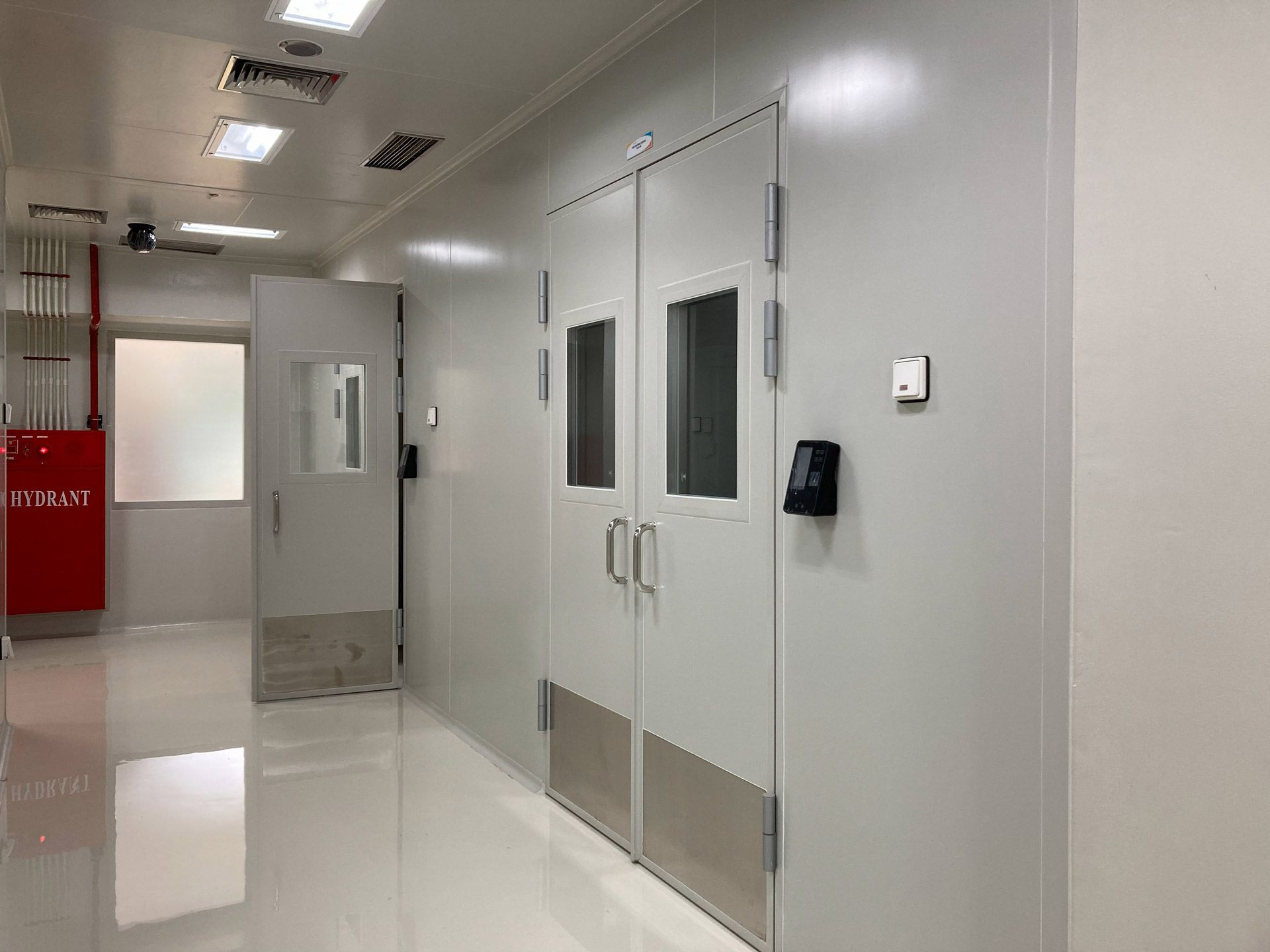 A clean, bright hallway in a laboratory or sterile facility featuring double doors, a fire cabinet, and clinical lighting.