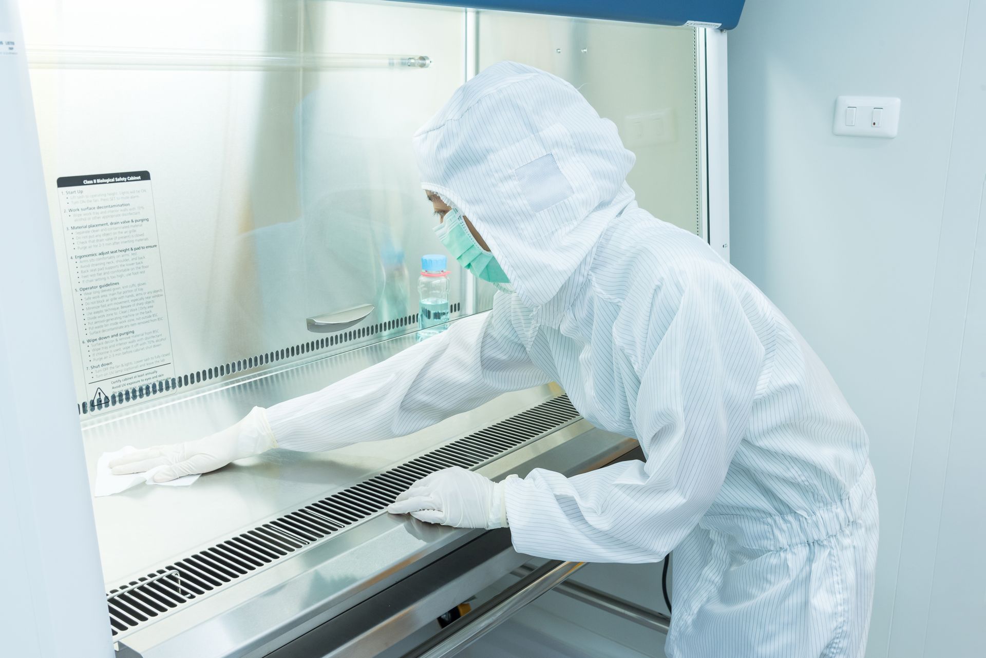 Person in a white protective suit cleans a laboratory hood. Person in a white protective suit cleans a laboratory hood.