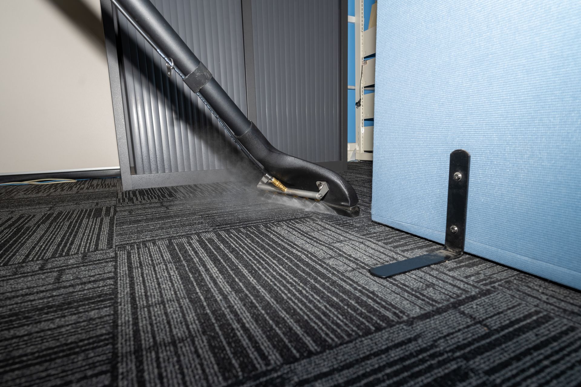 Carpet being cleaned with a vacuum. Black and gray striped carpet, black vacuum head, blue divider. Carpet being cleaned with a vacuum. Black and gray striped carpet, black vacuum head, blue divider.