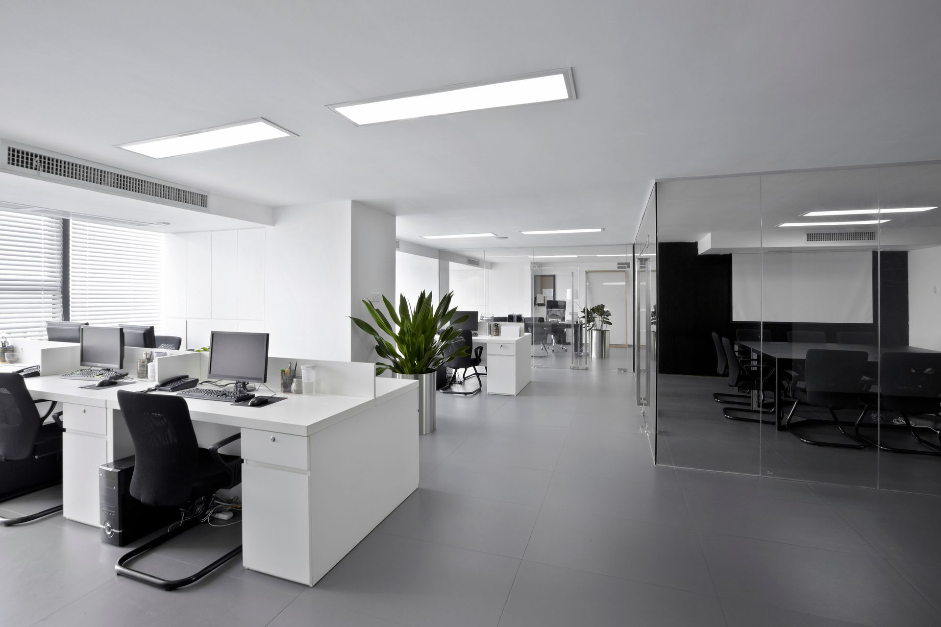 Modern office space with white desks, black chairs, and a glass-walled conference room.