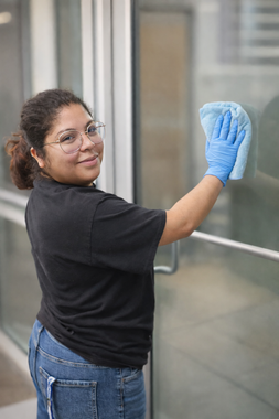 Window cleaner in blue overalls, using a squeegee on a large glass window.