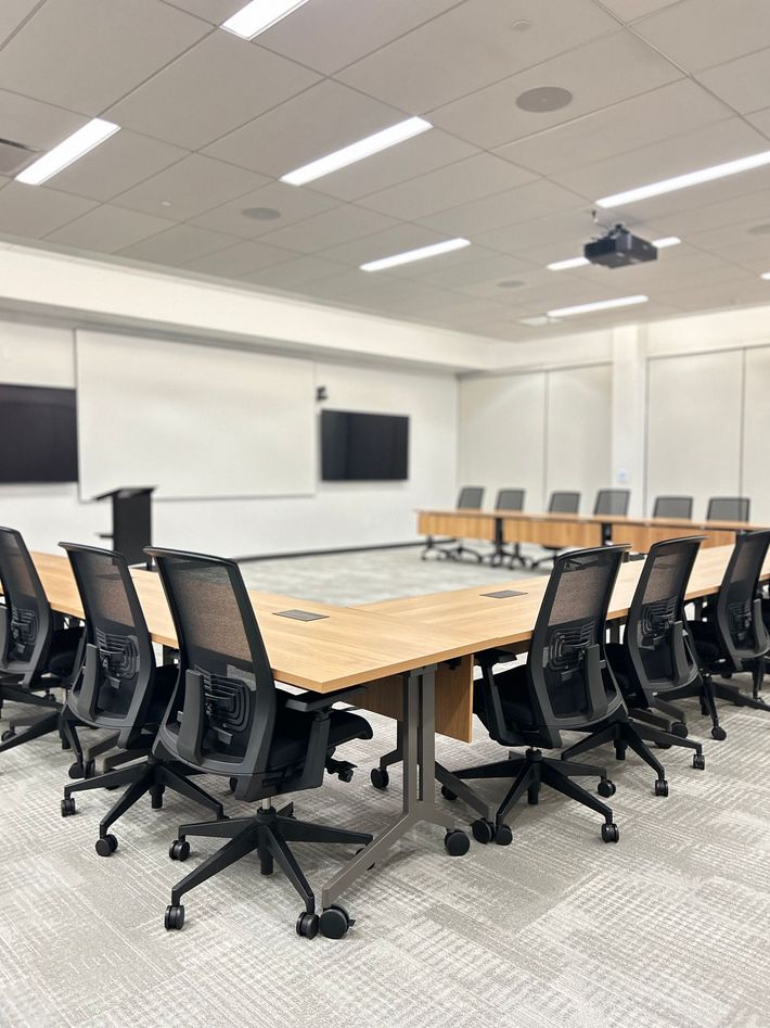 A conference room with a large wooden U-shaped table, black chairs