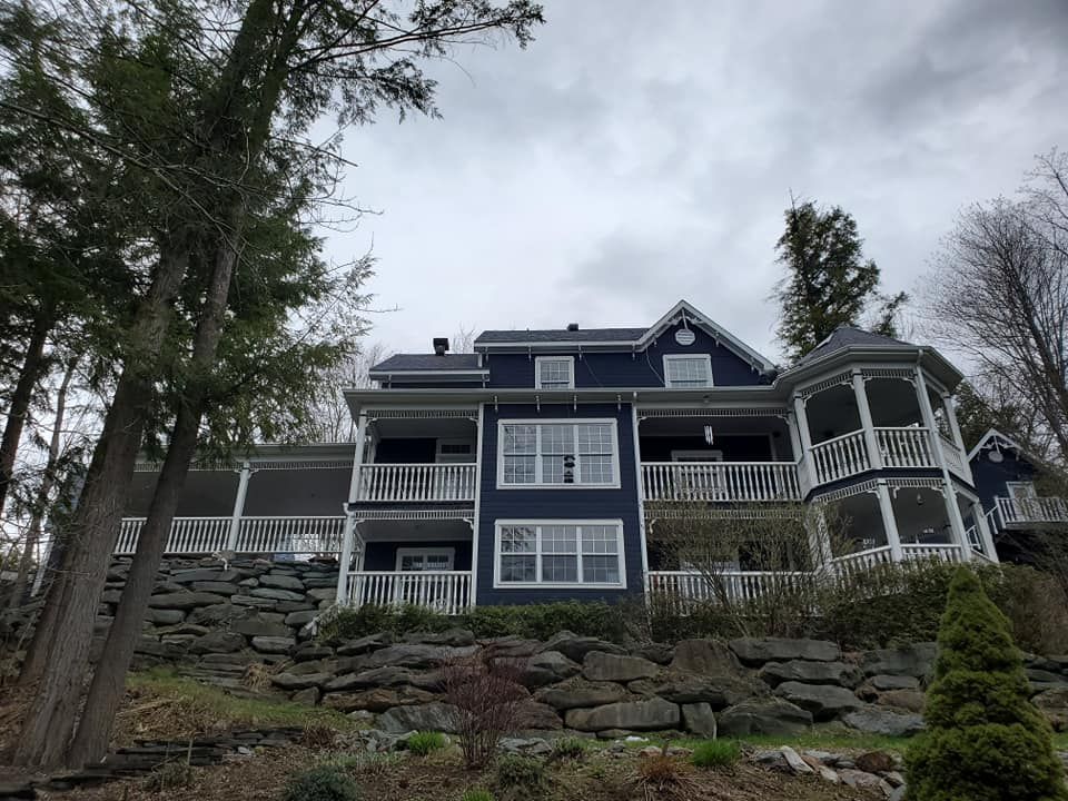 Maison bleue aux boiseries blanches, à plusieurs niveaux et dotée de vérandas enveloppantes, située à flanc de colline