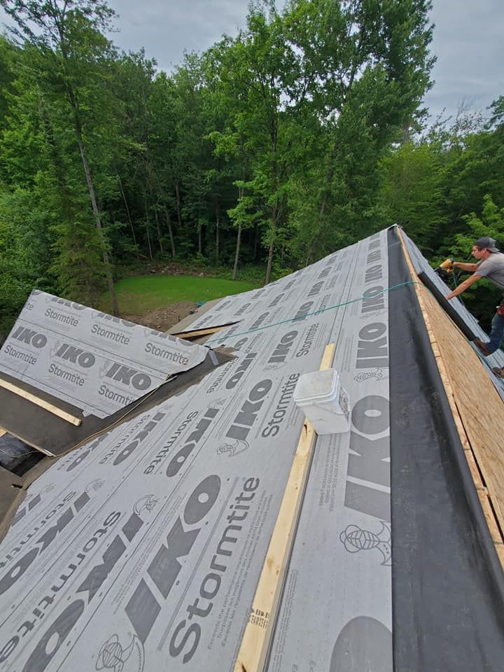 Travaux de toiture en cours ; pose d'une sous-couche grise Stormtite sur un toit, un ouvrier travaille dessus.