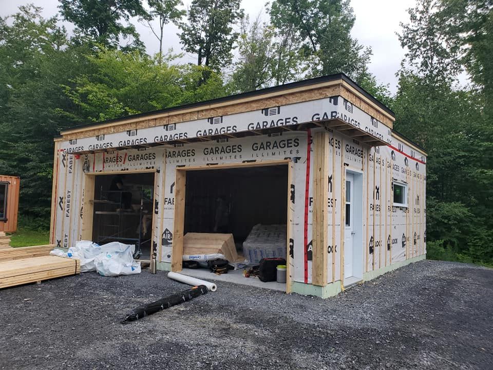 Garage en construction avec deux travées, une porte et une fenêtre ; sur une allée de gravier.