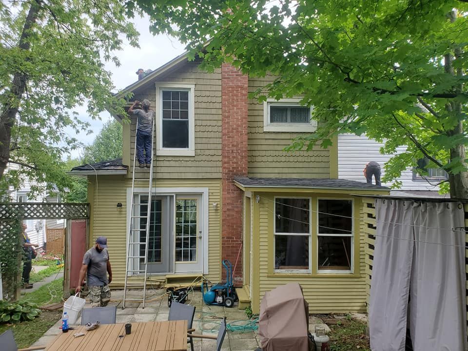 Des ouvriers réparent le toit et le revêtement d'une maison à deux étages avec une cheminée en briques.