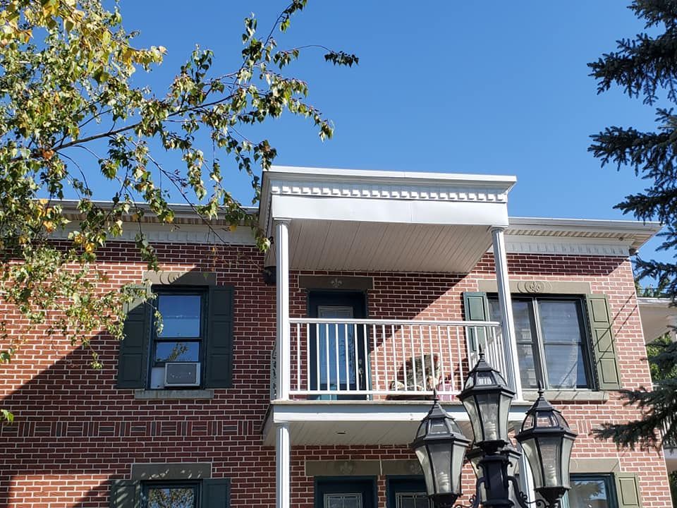 Immeuble en briques de deux étages avec balcon, volets vert foncé et ciel bleu clair.