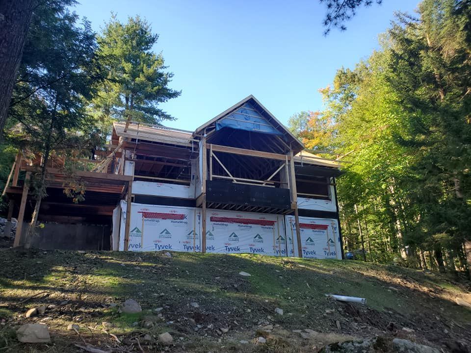 Maison en construction, charpente et revêtement visibles à flanc de colline.