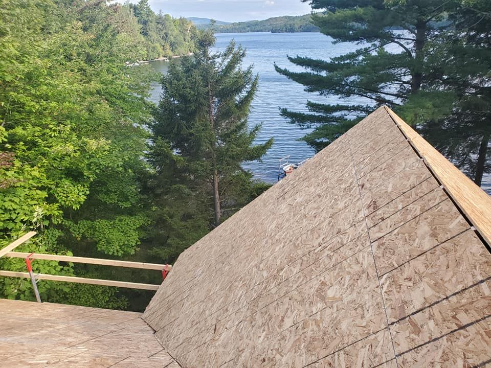 Toiture en construction, avec vue sur le lac et les arbres. Panneaux OSB apparents, non finis.
