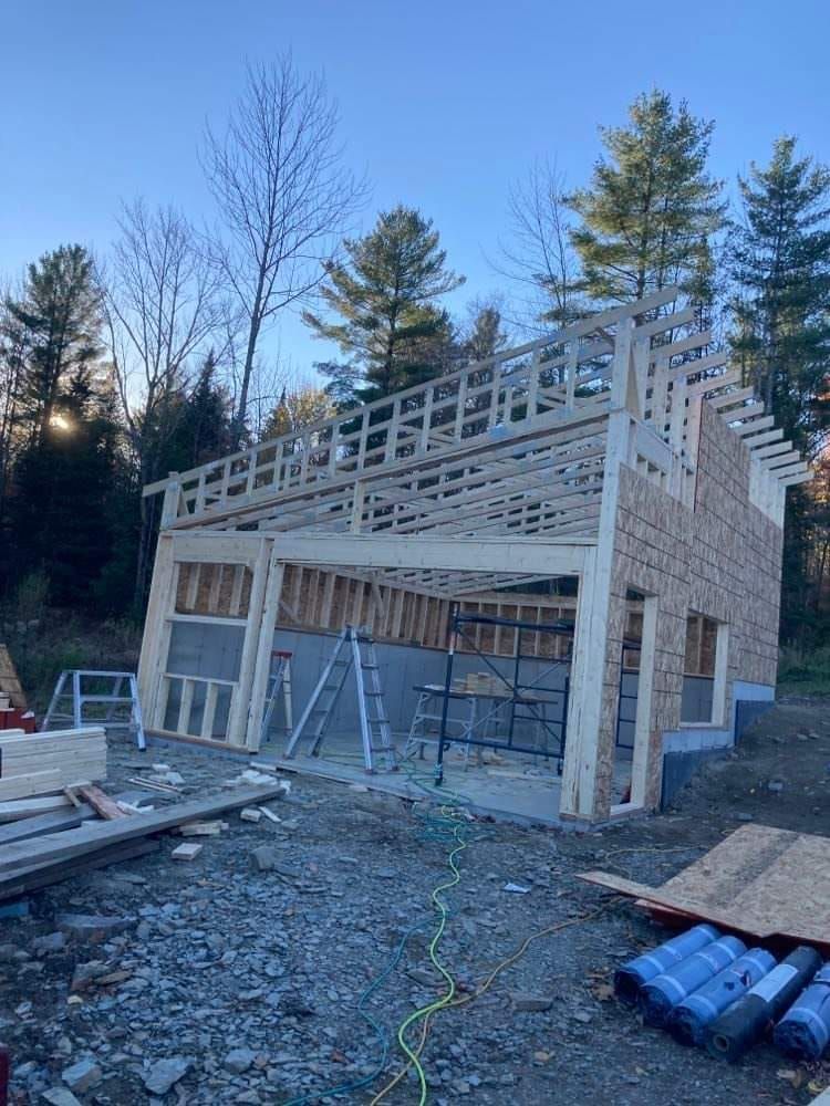 Garage en construction avec structure en bois, murs inachevés et échafaudages à l'extérieur.