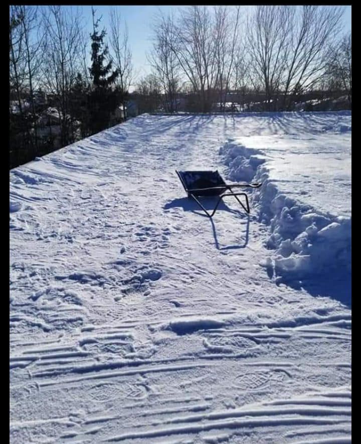 Toit enneigé avec une simple chaise ; arbres et ciel bleu en arrière-plan.