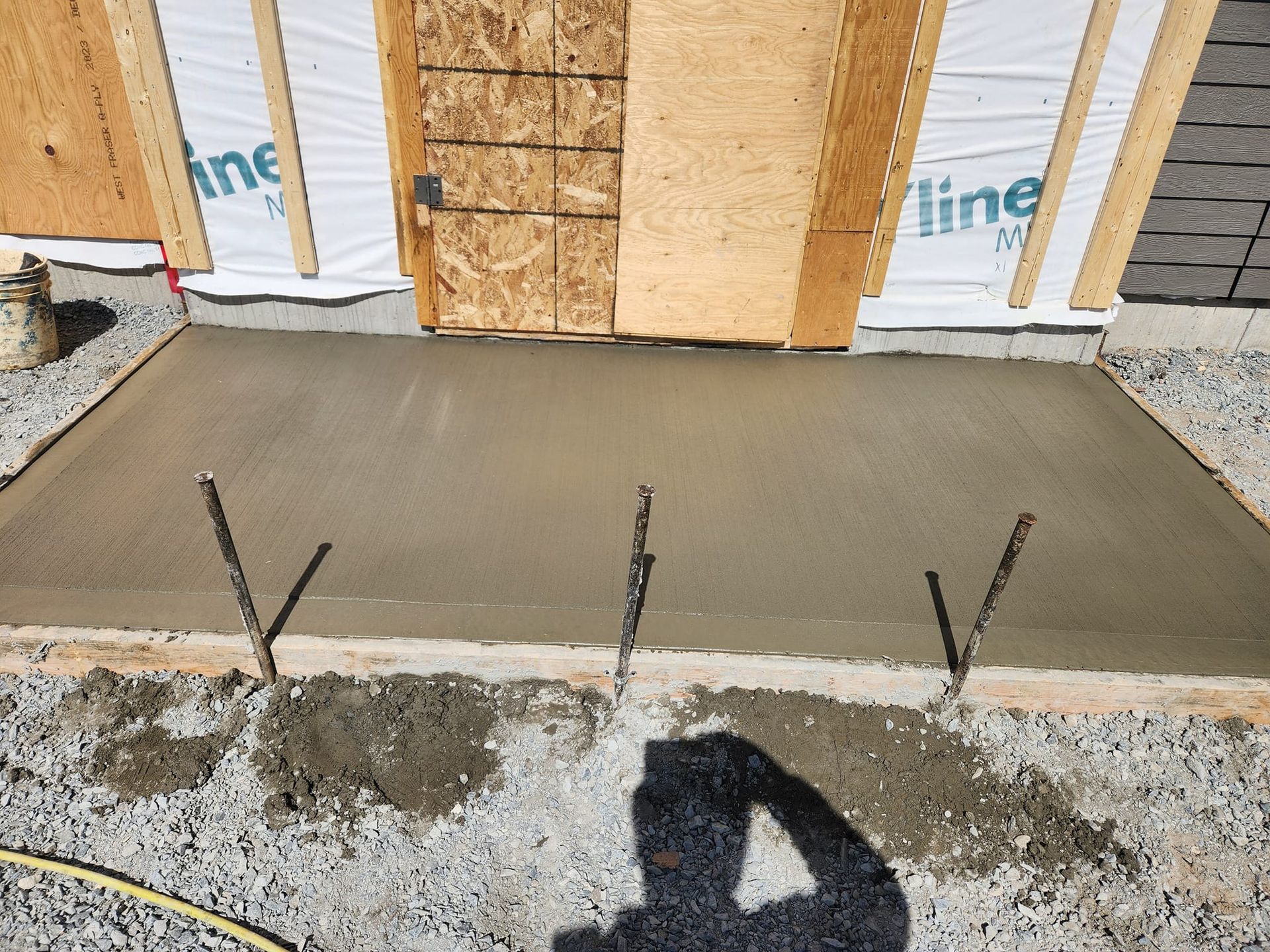 Dalle de béton fraîchement coulée avec armatures métalliques, sous une structure en bois.