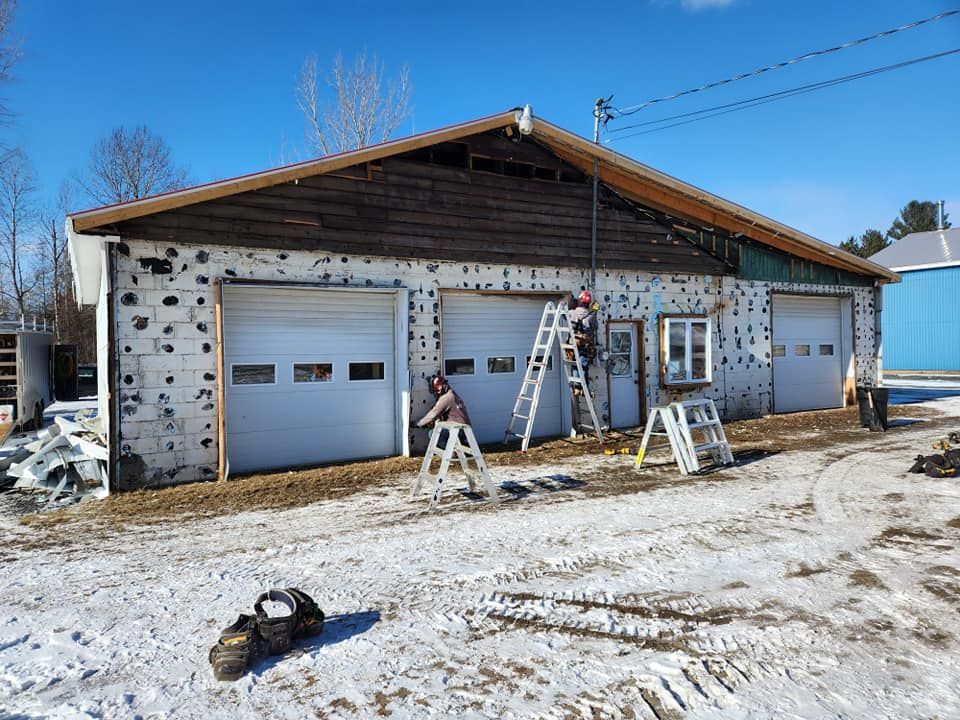 Garage à trois travées, des gens sur des échelles, de la neige au sol, ciel bleu.