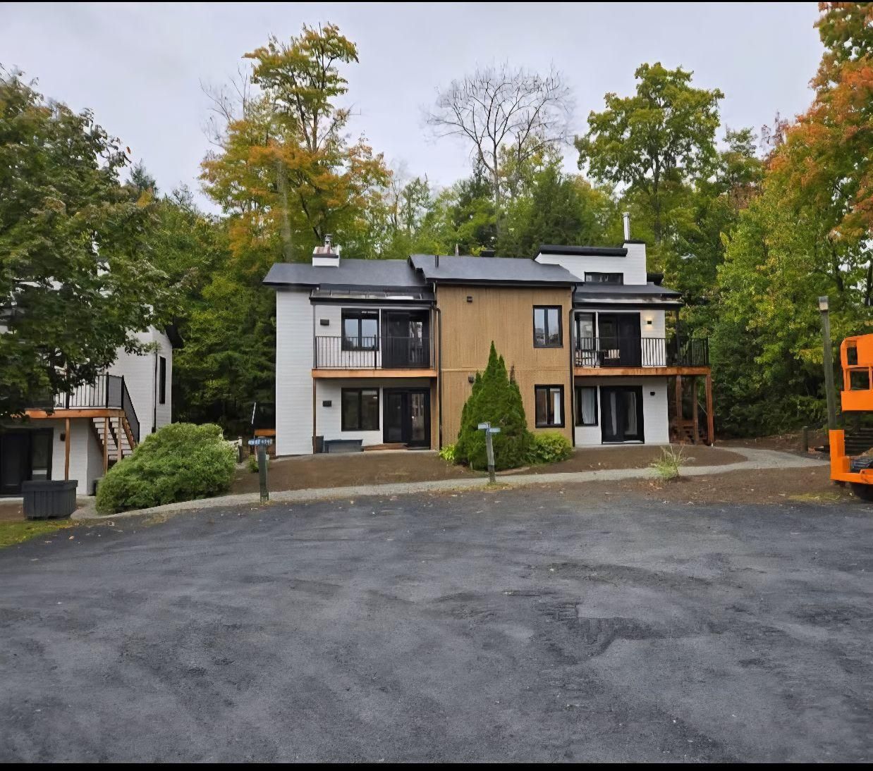 Maison moderne à deux étages avec toit foncé et bardage marron, entourée d'arbres.