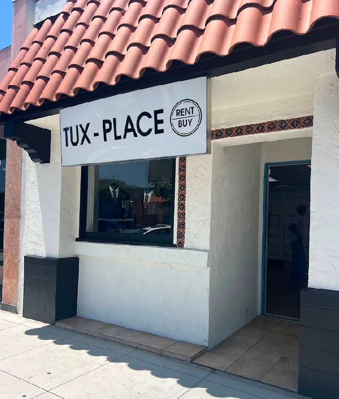 Storefront with a “TUX-PLACE” sign, white walls, and a red tiled roof.