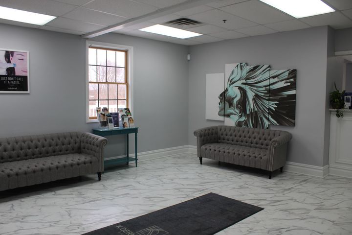 Modern waiting room with gray sofas, marble floor, wall art, and a small table by the window