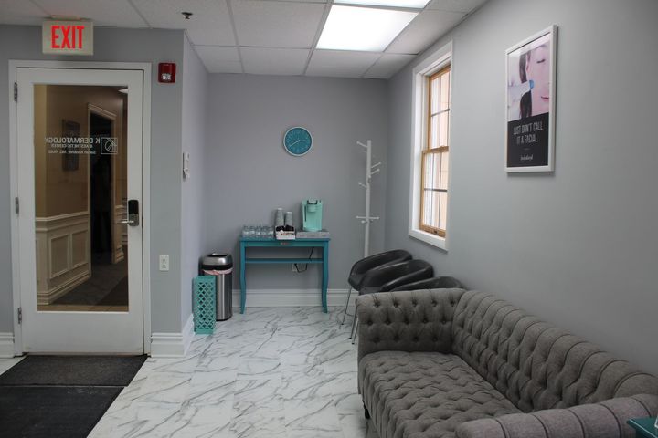 Modern clinic waiting room with tufted gray sofa, teal table, medical stand, window, and EXIT door