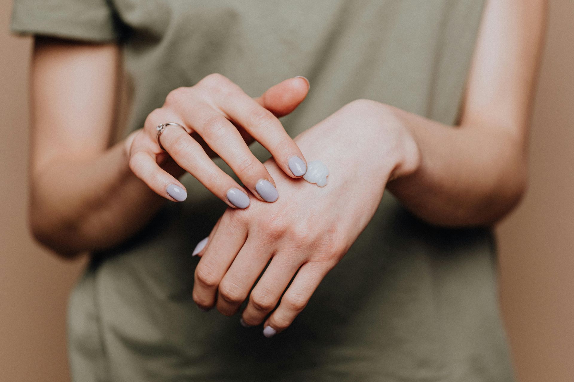 Close-up of hands with light blue nail polish, one hand gently touching the other against a neutral background