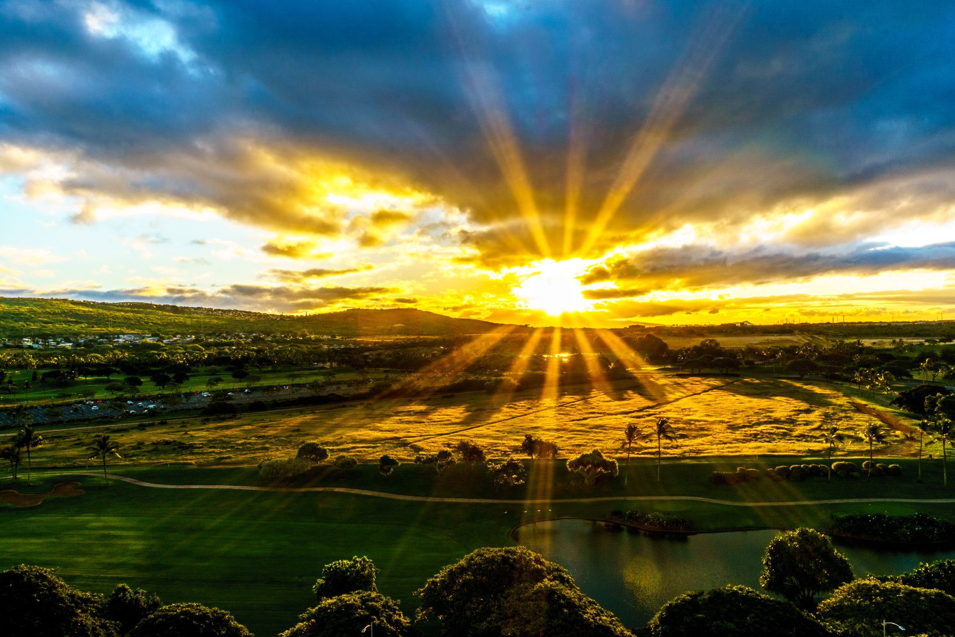 Golden sunset with rays of light, illuminating a landscape with trees, fields, and clouds.