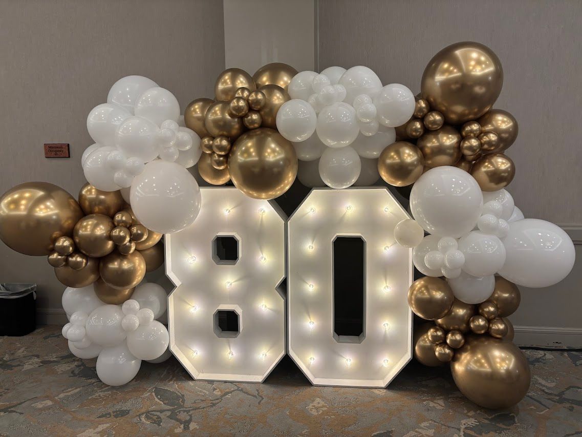 Gold and white balloon display with illuminated “80” numbers for a birthday celebration