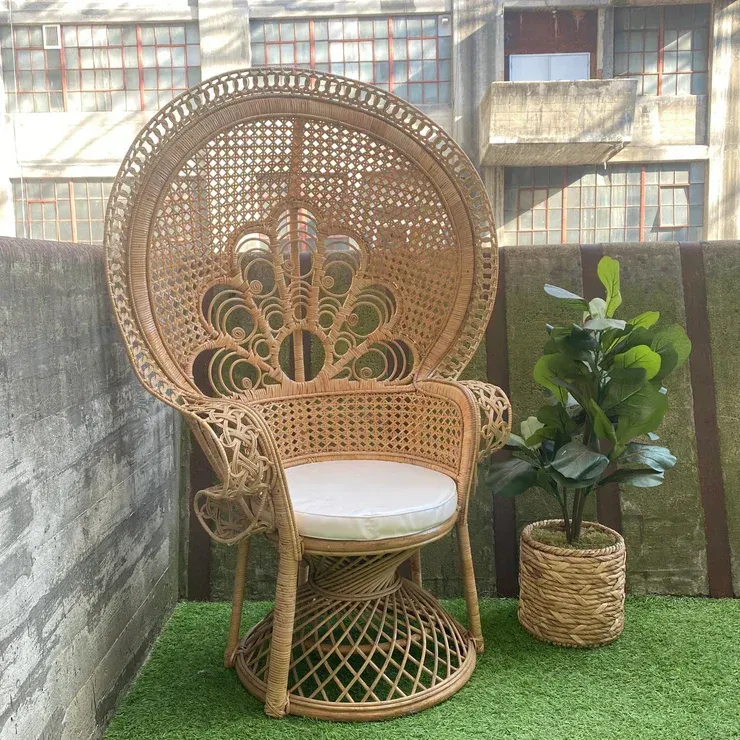A wicker chair is sitting in front of a wall with flowers on it.